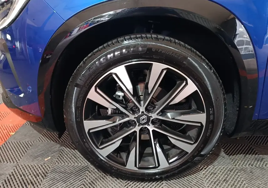 Gros plan sur la roue avant droite d’un Renault Austral bleu, jante alliage noire et argentée au design moderne.