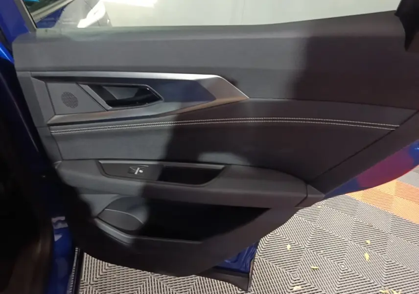Vue intérieure de la porte avant gauche du Renault Austral 2024 bleu, avec garniture noire et surpiqûres blanches.