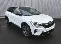 Renault Austral E-Tech Full Hybrid 200 Iconic blanc nacré avec toit noir, vue 3/4 avant sur sol humide, jantes alliage visibles.