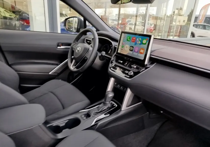 Intérieur avant du Toyota Corolla Cross 2025, tableau de bord noir avec écran tactile central et sièges tissu gris foncé.