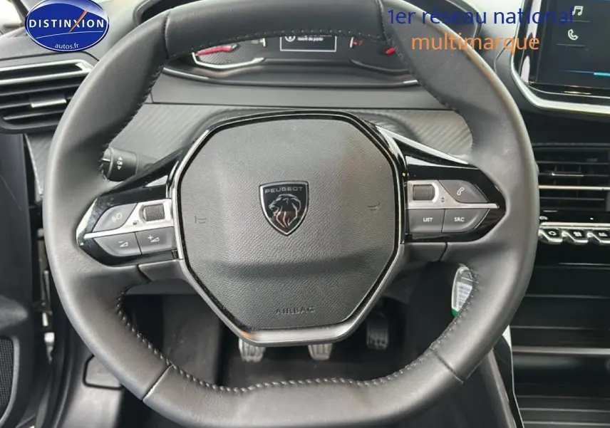 Vue rapprochée du volant noir de la Peugeot 208 1.2 PureTech 100 Active avec commandes intégrées et tableau de bord gris.