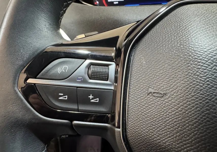 Gros plan sur les commandes gauche du volant cuir noir du Peugeot 3008 orange, avec boutons de volume et reconnaissance vocale.