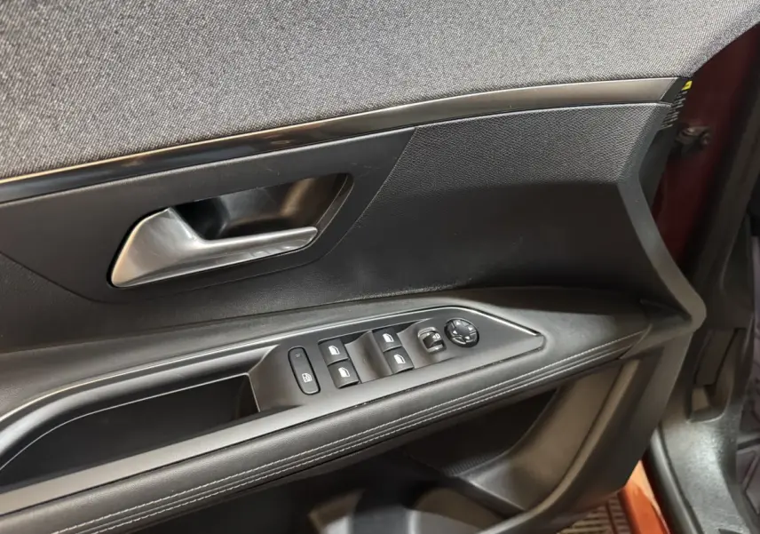 Vue rapprochée de la porte avant gauche de la Peugeot 3008 orange, montrant les commandes des vitres et le bouton de verrouillage.