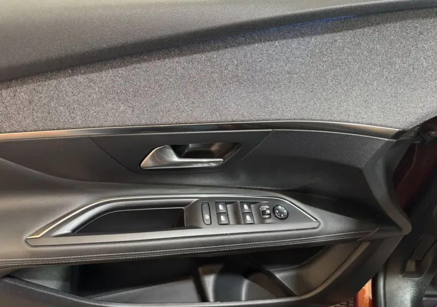 Intérieur côté gauche de la porte avant d’un Peugeot 3008 orange 2020, avec commandes des vitres et poignée argentée.