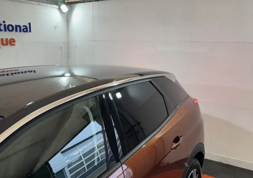 Vue 3/4 arrière droite du Peugeot 3008 orange avec toit noir et vitres teintées dans un garage.