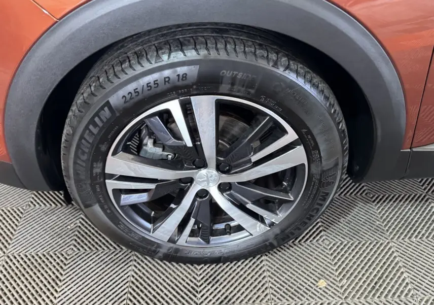 Gros plan sur la roue avant droite du Peugeot 3008 orange, mettant en valeur la jante alliage bicolore et le pneu Michelin.
