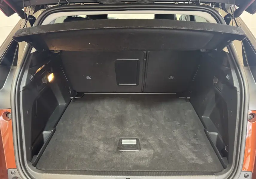 Coffre ouvert vu de l’arrière d’un Peugeot 3008 orange, espace de chargement propre avec cache-bagages déployé.