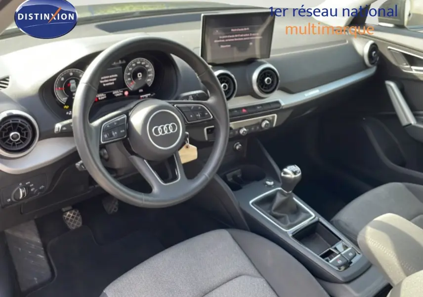 Vue intérieure côté conducteur de l'Audi Q2 30 TDI S-Line 2025, volant cuir, tableau de bord numérique et boîte manuelle.