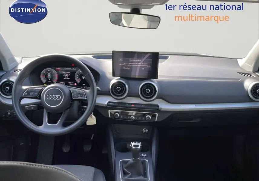 Vue intérieure avant de l'Audi Q2 30 TDI S-Line 2025, tableau de bord noir avec écran central et volant cuir multifonction.