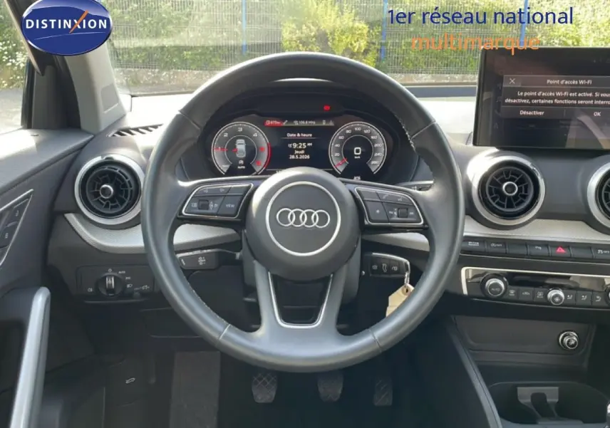 Vue intérieure frontale du volant cuir noir d’un Audi Q2 gris Manhattan, avec tableau de bord digital et écran tactile central.