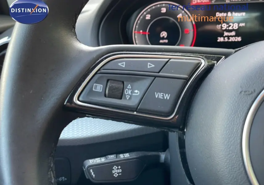 Gros plan sur le volant noir de l'Audi Q2 30 TDI S-Line 2025, avec commandes multifonctions et tableau de bord numérique en arrière-plan.