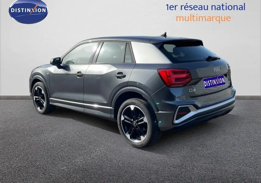 Audi Q2 30 TDI S-Line gris Manhattan métal, vue 3/4 arrière côté gauche, jantes noires distinctives.