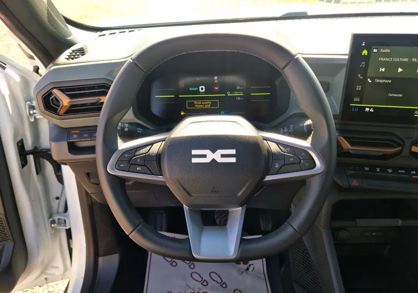 Vue intérieure centrée sur le volant du Dacia Duster blanc 2026, avec tableau de bord numérique et écran tactile visible.