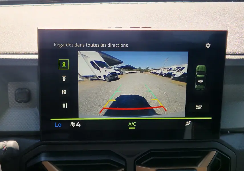 Vue arrière via caméra de recul du Dacia Duster blanc 2026, avec lignes de guidage colorées sur écran intérieur.