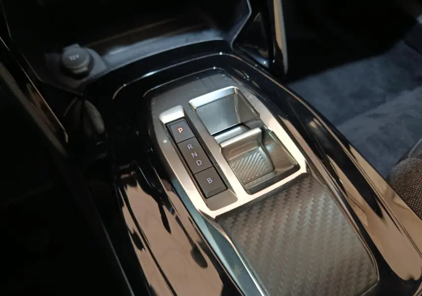 Gros plan sur la console centrale noire brillante avec sélecteur de vitesses électrique du Peugeot E-2008 gris clair.