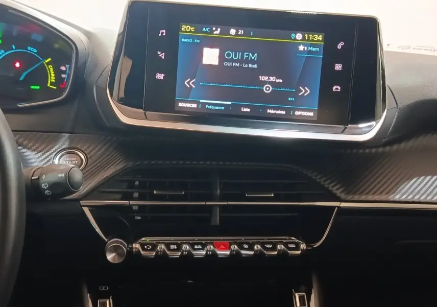 Vue rapprochée du tableau de bord de la Peugeot E-2008 électrique 2023 avec écran tactile central allumé et finition carbone.