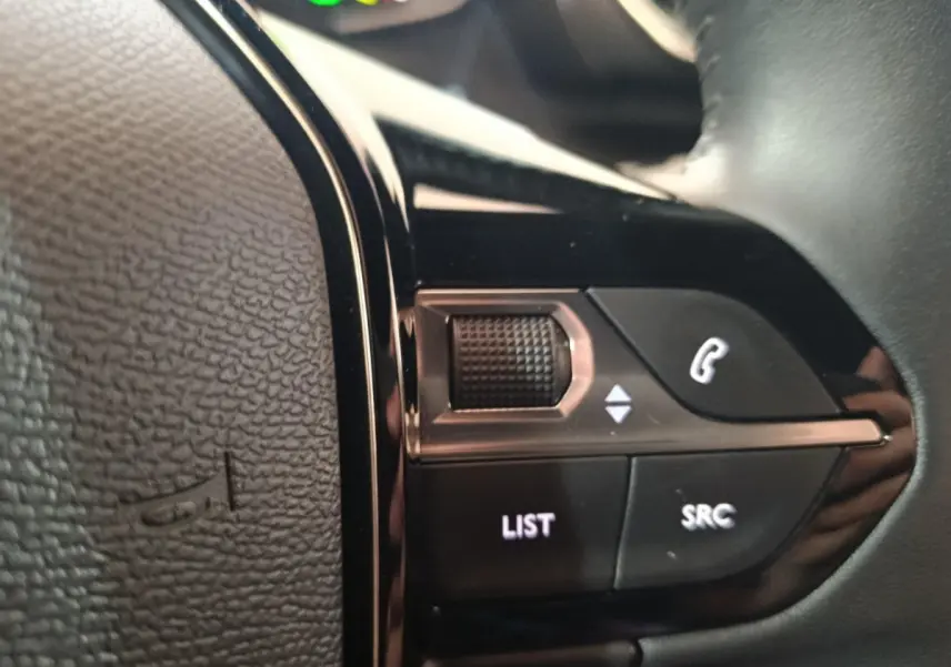 Gros plan sur les commandes multifonctions noires du volant cuir de la Peugeot E-2008 électrique gris clair.