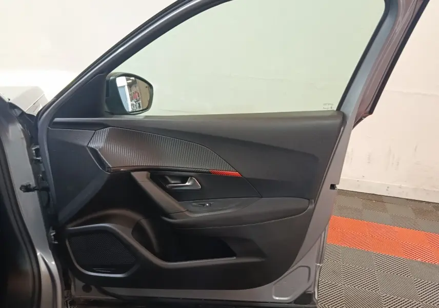 Vue intérieure de la porte avant gauche gris clair du Peugeot E-2008 électrique avec insert décoratif noir et rouge.