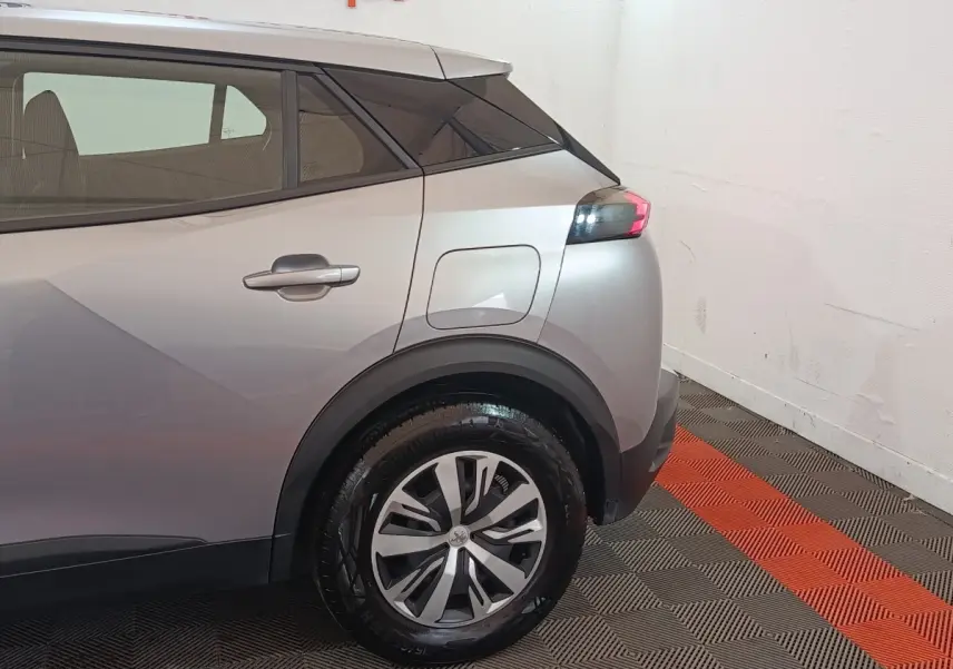Vue arrière côté droit du Peugeot E-2008 électrique gris clair, mettant en valeur la roue et le port de charge.