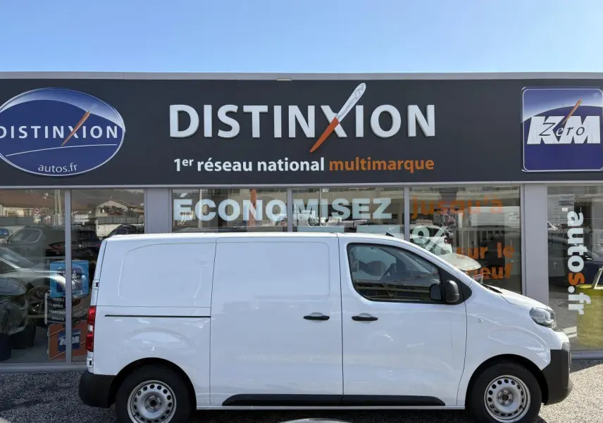Profil latéral droit d'un utilitaire Opel Vivaro blanc 2024 garé devant une concession Distinxion.