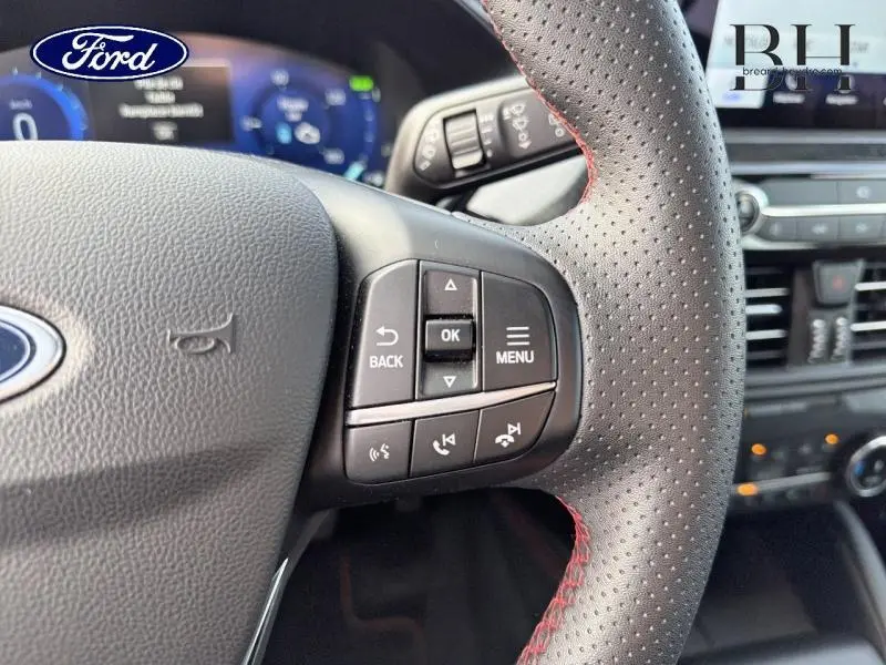 Gros plan sur le volant cuir perforé avec commandes multifonctions du Ford Kuga 2023, intérieur noir et rouge.