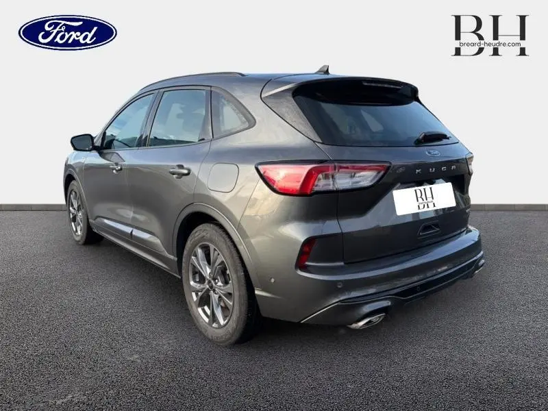 Ford Kuga gris métallisé vu en 3/4 arrière droit, avec hayon mains libres et double sortie d'échappement chromée.