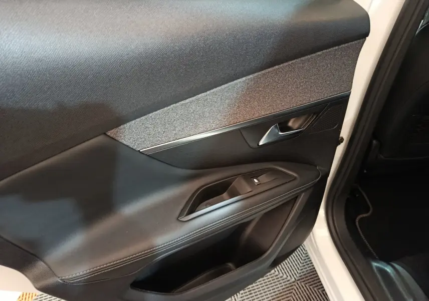 Gros plan sur la porte avant droite noire avec poignée argentée et bouton de lève-vitre d’un Peugeot 3008 blanc.