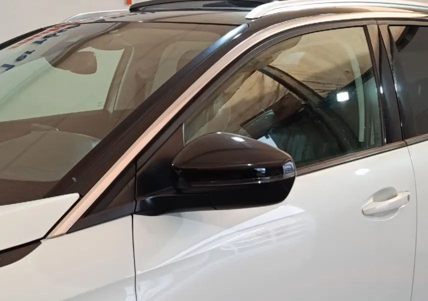 Vue rapprochée côté gauche avant d’un Peugeot 3008 blanc avec rétroviseur noir brillant et toit panoramique.