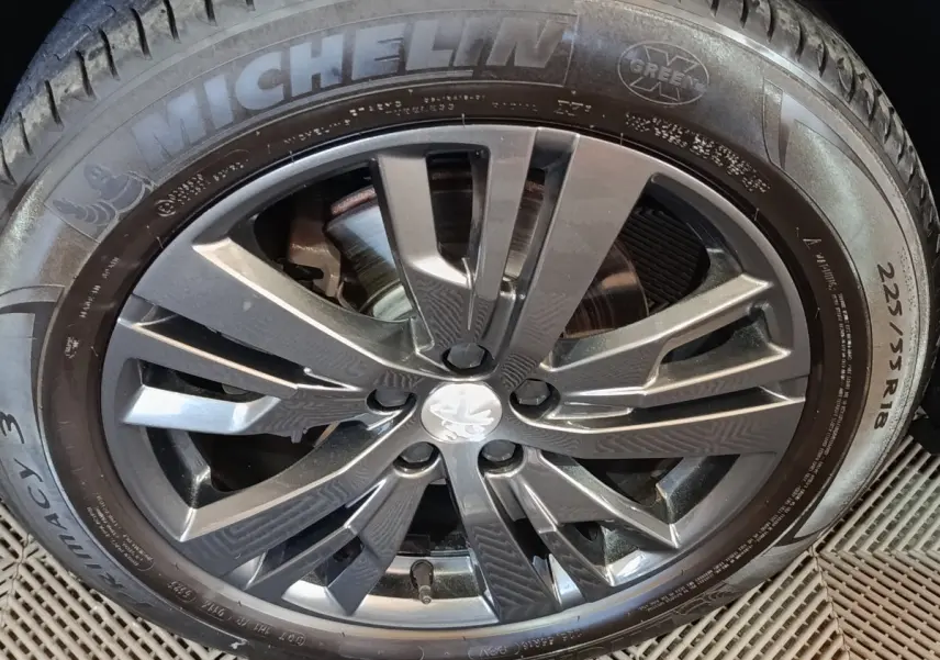 Gros plan sur la jante alliage gris foncé et pneu Michelin 225/55 R18 du Peugeot 3008 blanc, version Puretech 130.
