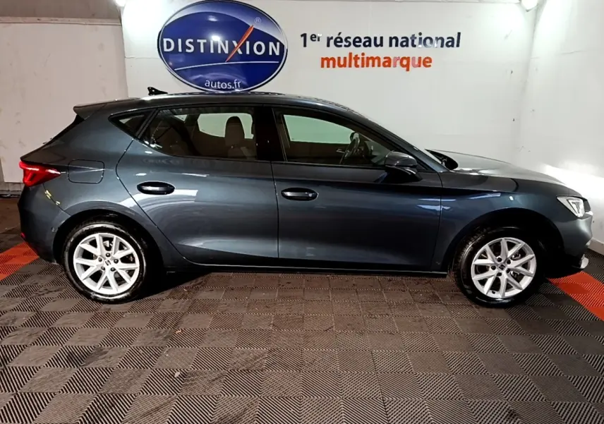 Vue de profil côté gauche d'une SEAT Leon gris clair 2023, avec jantes alliage et feux arrière LED visibles.