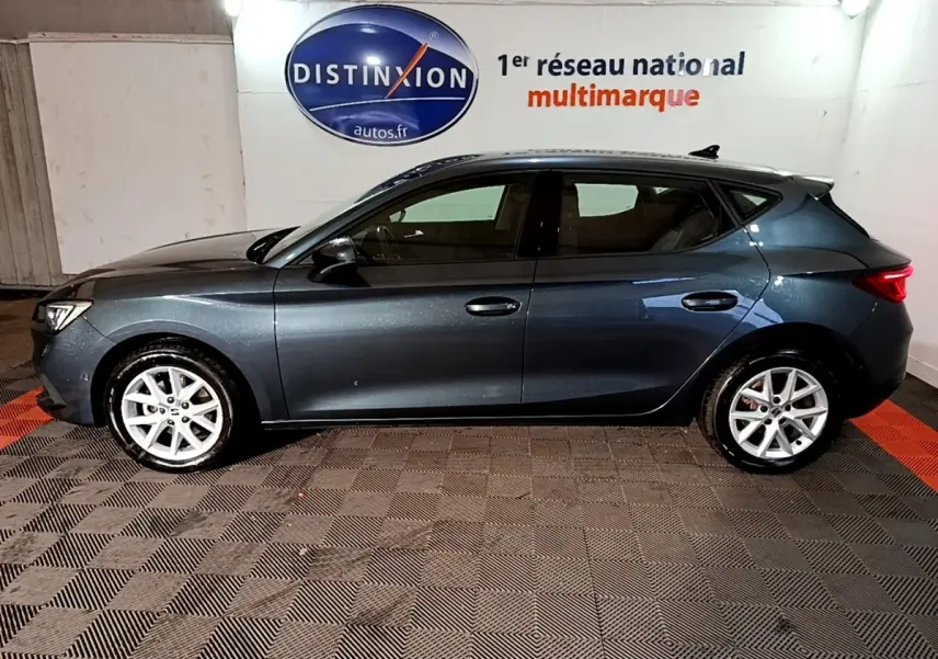 Vue de profil côté gauche d'une SEAT Leon gris clair 2023, avec jantes alliage et éclairage intérieur ambiant visible.