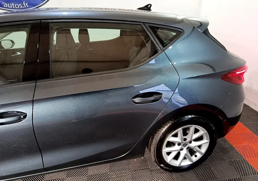 Vue côté droit arrière d'une SEAT Leon gris clair métallisé avec jantes alliage et feux arrière allumés.