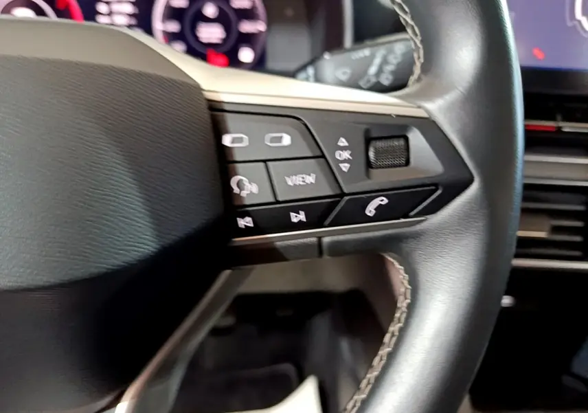 Gros plan sur les commandes gauche du volant cuir du SEAT Leon 2023, avec tableau de bord numérique en arrière-plan.