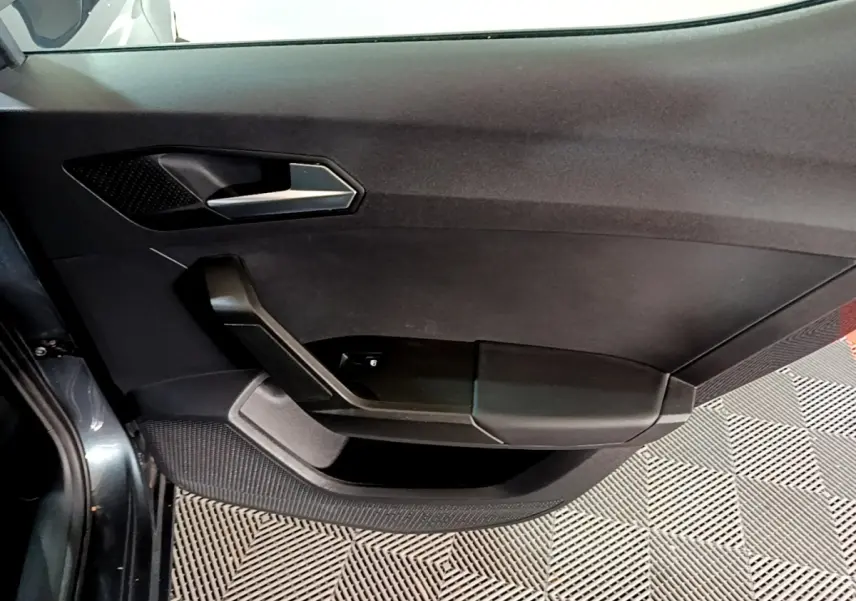 Vue intérieure du panneau de porte côté gauche gris foncé du SEAT Leon 2023 avec poignée argentée et commandes électriques.