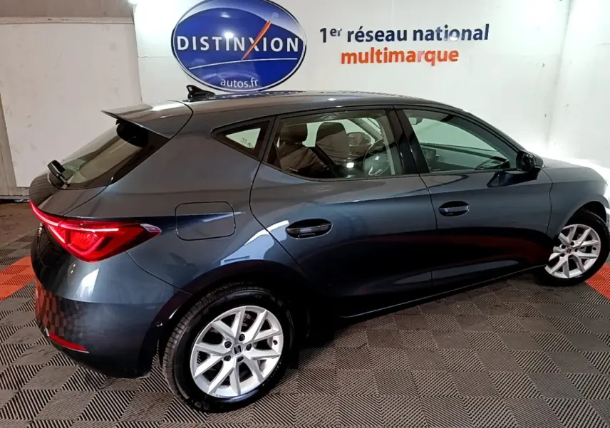 Vue côté droit arrière d'une SEAT Leon gris clair 2023 avec feux arrière LED et jantes alliage.