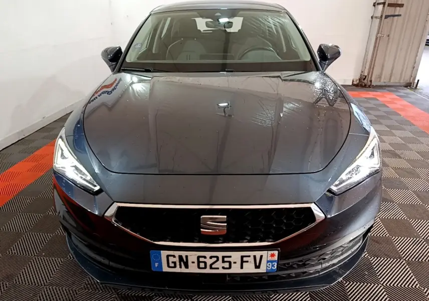 Vue avant d'une SEAT Leon gris clair 2023 avec phares LED allumés dans un garage fermé.