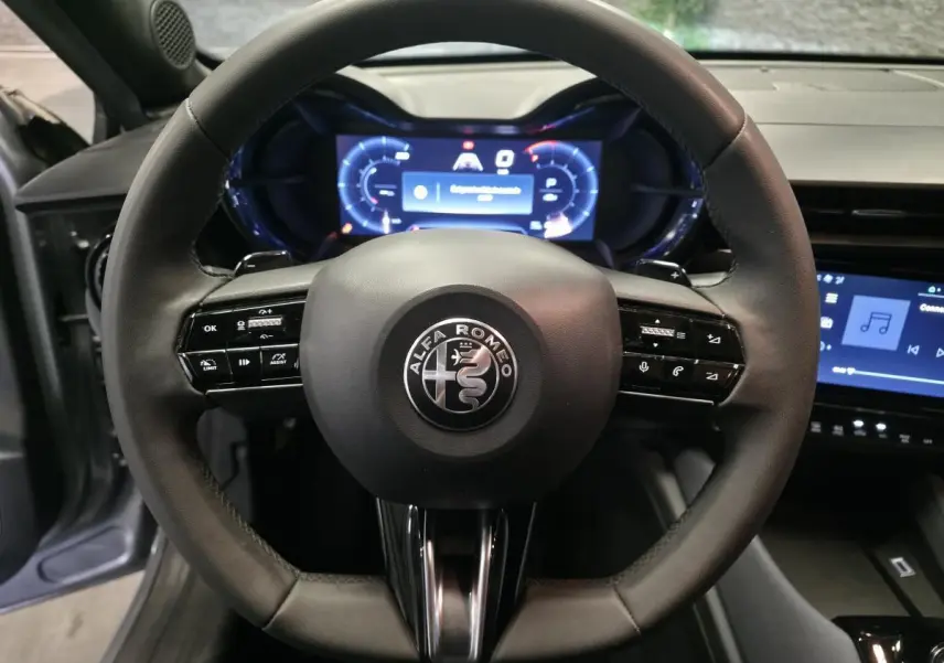 Vue rapprochée du volant noir multifonctions de l'Alfa Romeo Junior 2025 avec tableau de bord digital lumineux.