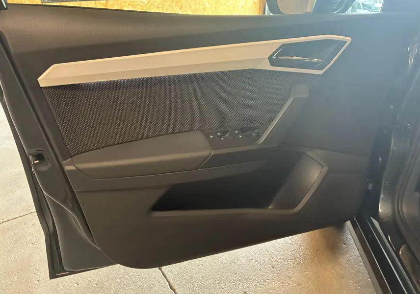 Vue intérieure de la porte avant gauche d'une SEAT Arona gris foncé, avec commandes de vitres et poignée intégrée.