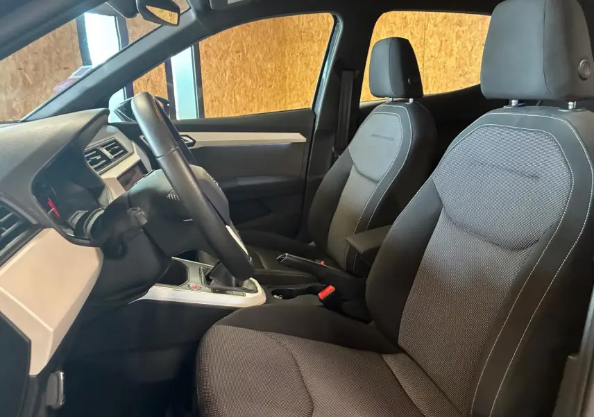 Vue intérieure côté conducteur du SEAT Arona gris foncé 2021, sièges tissu noir et tableau de bord moderne.