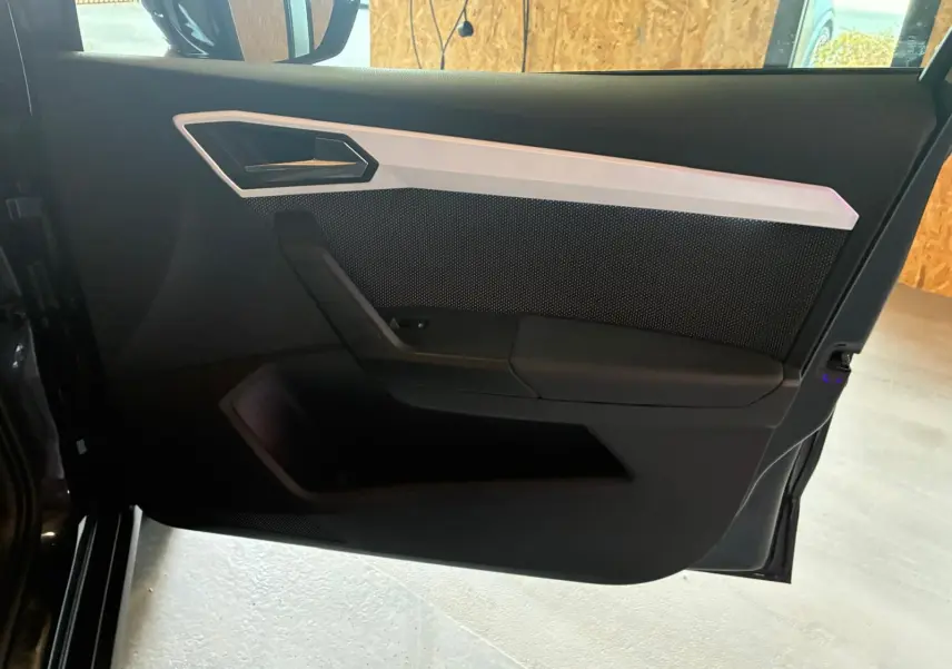 Vue intérieure de la porte avant gauche du SEAT Arona gris foncé, avec garniture noire et insert argenté.