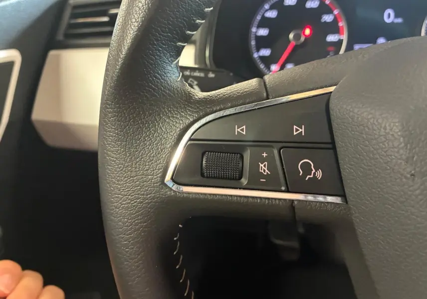 Gros plan sur les commandes audio au volant du SEAT Arona 1.0 TSI 110 Xcellence, intérieur noir avec tableau de bord visible.