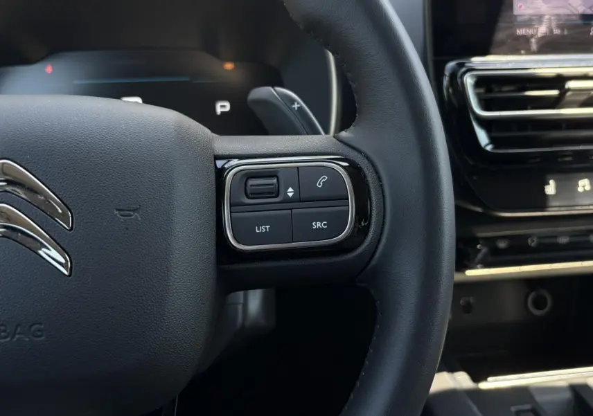 Gros plan sur le volant noir du Citroën C5 Aircross Hybrid 2025, avec commandes intégrées et palettes au volant visibles.