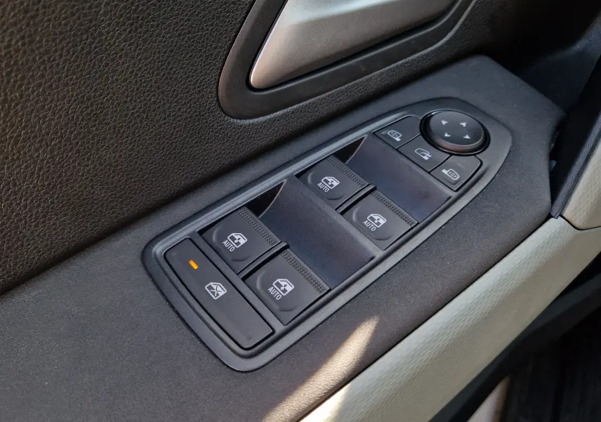 Gros plan sur les commandes de lève-vitres et rétroviseurs côté conducteur du Dacia Duster blanc, intérieur noir et beige.