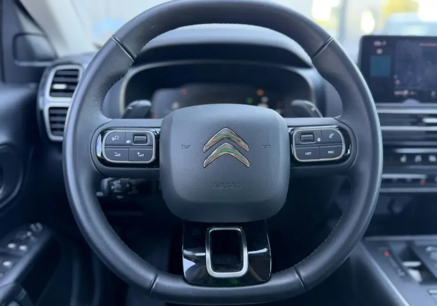 Vue rapprochée du volant cuir noir du Citroën C5 Aircross 2025 avec commandes intégrées et logo chromé central.