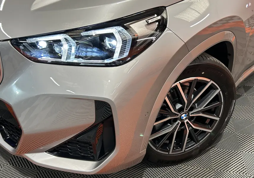 Gros plan sur l'avant droit d'un BMW X1 Spacesilber 2024, mettant en valeur le phare LED et la jante M Sport noire.