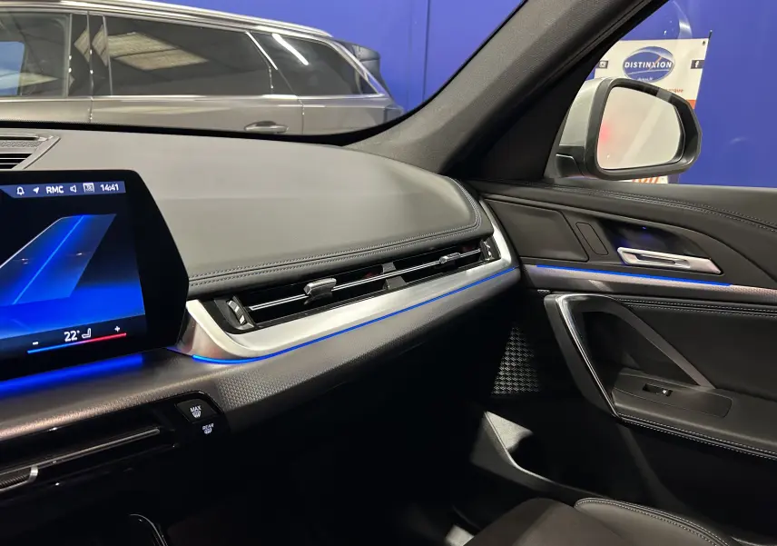 Intérieur avant droit du BMW X1 2024 Spacesilber, tableau de bord M Sport avec éclairage d'ambiance bleu et finitions cuir.