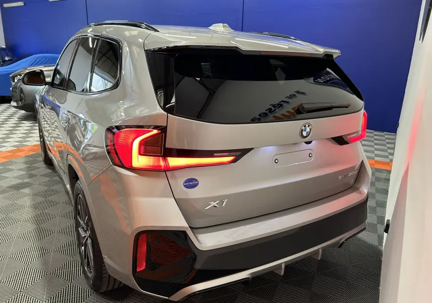 Vue 3/4 arrière gauche d'un BMW X1 2024 Spacesilber avec feux LED allumés et vitres teintées.