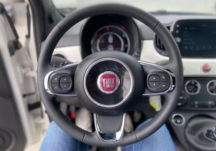 Vue rapprochée du volant noir de la Fiat 500 blanche 2024 avec commandes intégrées et tableau de bord visible.