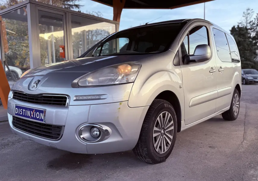 Vue 3/4 avant droit d'un Peugeot Partner Tepee gris 2014 avec phares allumés et jantes spécifiques Family.