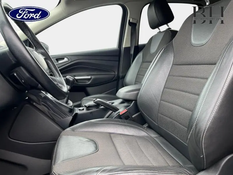 Vue intérieure côté conducteur du Ford Kuga 2015, sièges sport en cuir et tissu gris avec volant multifonction cuir.